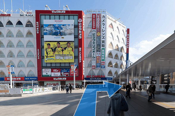 東口を出てビックカメラの方へ進み、ビックカメラ手前で右へ曲がります。